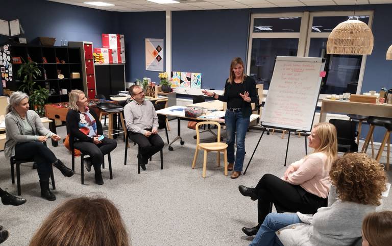 Group of people gathered in a circle and listening woman presenting.